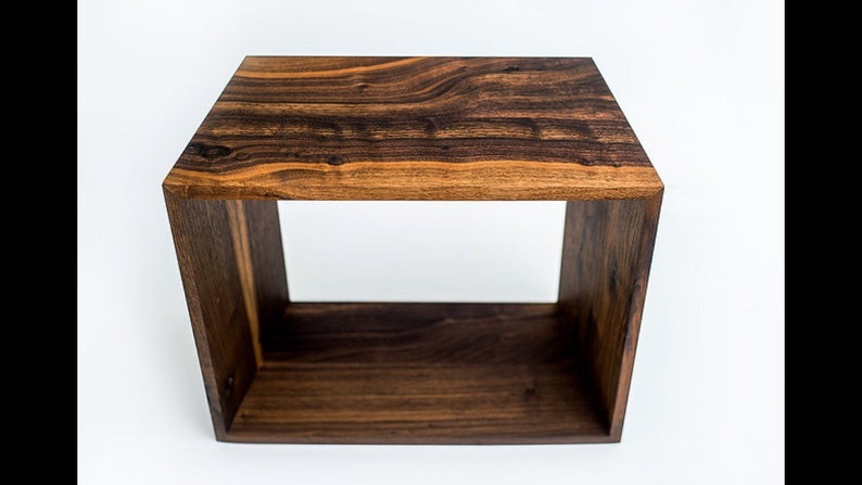 May include: A dark brown wooden cube-shaped end table with a wide, open shelf. The table is made of solid wood with a natural wood grain pattern.
