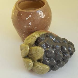May include: A ceramic pot with brown and white glaze, and a ceramic grape cluster with green leaves.