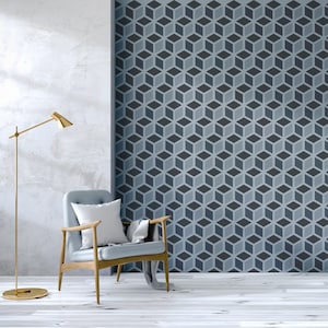 May include: A light blue armchair with a white cushion and a throw blanket sits in a room with a white wall and a wall with a geometric pattern of blue and grey cubes. A gold floor lamp stands to the left of the chair.