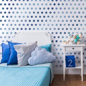 May include: A white bed with a blue and white patterned headboard and a blue and white patterned duvet cover. The bed has a blue cloud-shaped pillow and a grey and white patterned pillow. There is a white bedside table with a blue box labelled "2" on it. The bedside table has a bowl of white and blue balls on it.