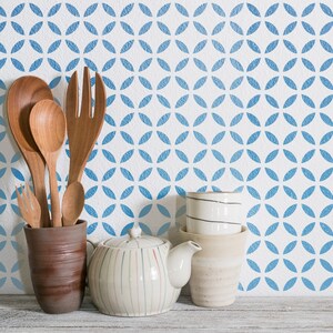 May include: A selection of kitchen and serving items. Features wooden spoons, a fork, and a small fork in a brown ceramic pot. A white teapot with vertical stripes and stacked ceramic cups are also visible.