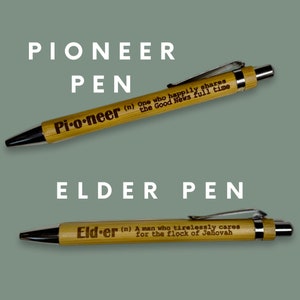 May include: Two wooden pens with engraved text. The top pen reads "Pioneer (n) One who happily shares the Good News full time". The bottom pen reads "Elder (n) A man who tirelessly cares for the flock of Jehovah".