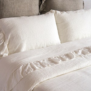 May include: White linen bedding with ruffled edges. The bedding is made of soft, natural linen and has a relaxed, casual look.