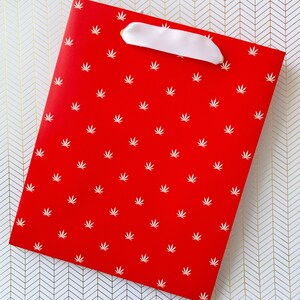 K&ouml;nnte beinhalten: Rote Geschenkt&uuml;te mit wei&szlig;em Band und wei&szlig;em Blattmotiv.