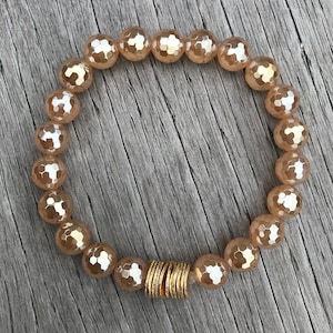 May include: A peach-colored beaded bracelet with a gold accent. The beads are faceted and have a shimmery finish.