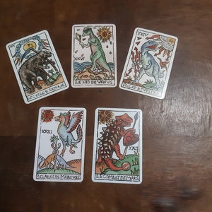 May include: Five tarot cards with illustrations of dinosaurs and mythical creatures. The cards are from a deck called "Le Cycle de Saturne", "Le Nid de Venus", "Eclat de Jupiter", "Les Ailes de Mercure", and "Le Combat de Mars".