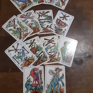 May include: A set of 12 tarot cards featuring colorful illustrations of dinosaurs and bones. The cards are numbered from II to VIII and X, with the words "Roy-de-Fossiles", "Chevalier-de-Fossiles", and "Reyne-de-Fossiles" on three of the cards.
