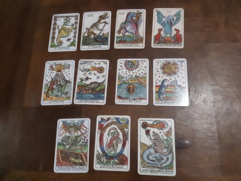 May include: A set of 12 tarot cards featuring colorful illustrations of dinosaurs and related themes. The cards are numbered from I to XII and include titles such as "Le Tyran," "La Spinosaurus," and "L'Extinction."