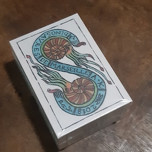 May include: A deck of tarot cards with a white background and a colorful illustration of two nautilus shells. The text on the card reads "Tarot de Marseille".