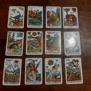 May include: A set of 10 tarot cards featuring colorful illustrations of dinosaurs. Each card has a Roman numeral and a title in French. The cards are printed on thick cardstock and have a matte finish.