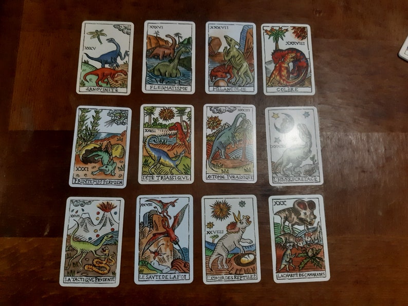 May include: A set of 10 tarot cards featuring colorful illustrations of dinosaurs. Each card has a Roman numeral and a title in French. The cards are printed on thick cardstock and have a matte finish.