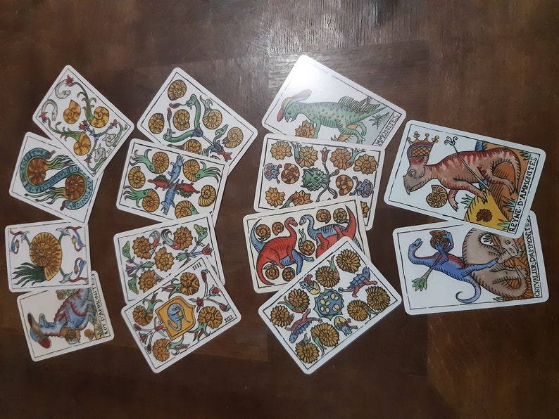 May include: A set of 10 tarot cards featuring colorful illustrations of dinosaurs and other creatures. The cards are laid out on a wooden surface. The cards are from the "Tarot of the Amazons" deck.