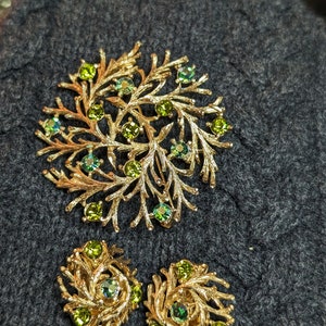 May include: A gold-tone brooch and earrings set with a leafy design and green rhinestones.