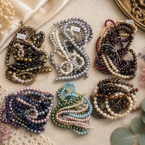 May include: Six coiled strands of round beads in various colors including metallic bronze, silver, deep red, dark blue, light blue, and cream. Each strand is arranged in a circular pattern, featuring small, uniform spherical beads on thin wire.