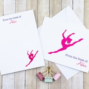 May include: White stationery set featuring a fuchsia gymnast silhouette. The set includes a notepad and a card with the text "From the Desk of: Abbie". A set of colorful paper clips is at the bottom.