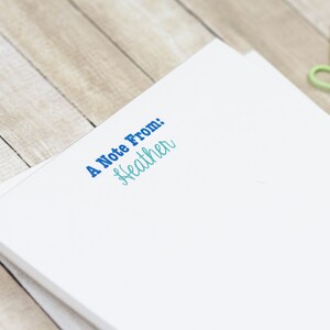 May include: A white notepad with the text "A Note From: Heather" printed in blue and teal.