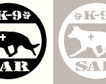 Op de afbeelding: Zwart-wit rond logo met een silhouet van een Duitse herder die rent met een plusteken aan zijn zijde. De tekst "K-9" staat boven de hond en "SAR" onder de hond.