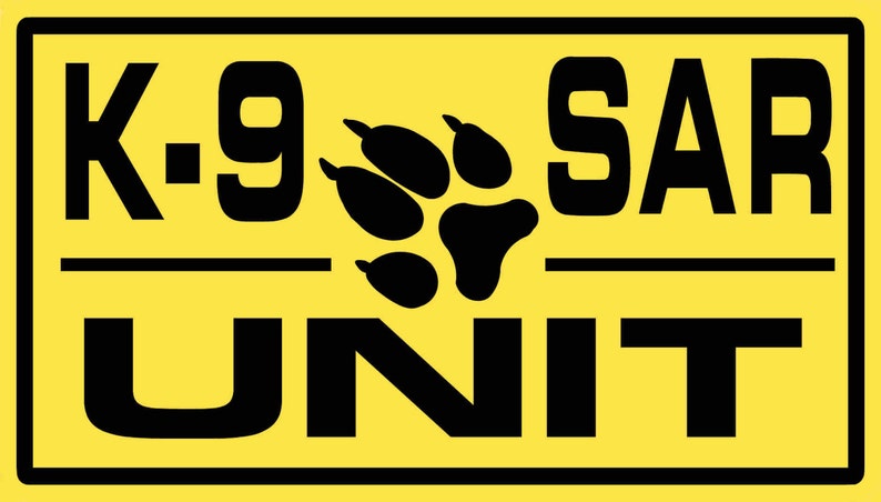 Peut inclure: Un panneau jaune avec du texte noir et une empreinte de patte qui dit "K-9 SAR UNIT".