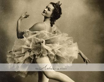 Op de afbeelding: Sepia-getinte vintage foto van een ballerina in een tutu, midden in een dans. Ze draagt een kroon en balletschoenen, met één been uitgestrekt. De tutu is gelaagd en volumineus, wat een gevoel van beweging en gratie creëert.