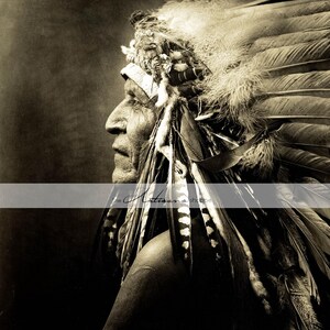 May include: Sepia-toned portrait of a Native American man in profile, wearing a feathered headdress. The headdress features large, layered feathers and intricate detailing. The man's face shows age and wisdom, with a strong nose and weathered skin. The image is a close-up, focusing on the man's face and headdress.