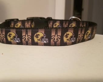 Könnte beinhalten: Ein schwarzes und goldenes Hundehalsband mit einem sich wiederholenden Muster aus Fußbällchen und Fleur-de-lis.