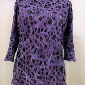 May include: Purple and black patterned sweater with a loose fit and 3/4 sleeves. The sweater has a unique design with cutouts that create a lace-like effect.