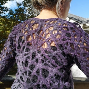 May include: Purple sweater with a black lace pattern. The sweater has a loose fit and long sleeves.