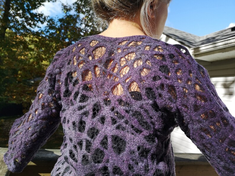 May include: Purple sweater with a black lace pattern. The sweater has a loose fit and long sleeves.
