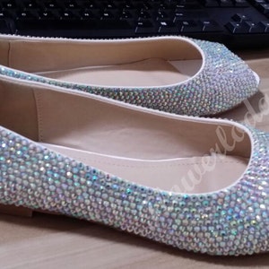 Op de afbeelding: Een paar witte peeptoe ballerina's bedekt met iriserende strass steentjes.