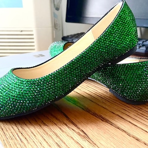 Puede incluir: Un par de zapatos planos de color verde esmeralda cubiertos de pedrería. Los zapatos son de punta y tienen un tacón bajo.
