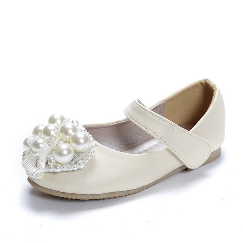 Puede incluir: Zapatos blancos de cuero para ni&ntilde;as con un adorno de coraz&oacute;n de perlas en la punta.