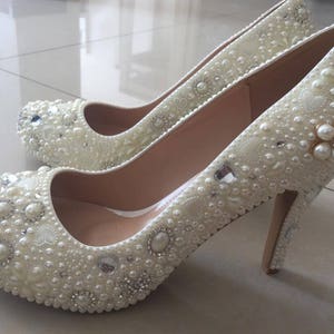 Può includere: Scarpe bianche con tacco alto con decorazioni di perle e strass.