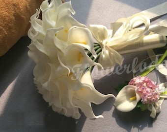 May include: A white bridal bouquet of artificial calla lilies with a satin ribbon and a matching boutonniere with pink flowers.