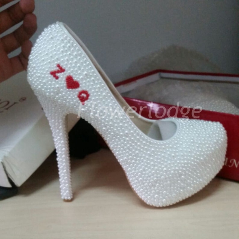 May include: White high-heeled shoes covered in white pearls with a red heart and the letters "Z" and "Q" embroidered on the side.