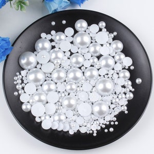 May include: A black plate filled with white pearl beads of various sizes. The pearls are a mix of round and flat shapes.