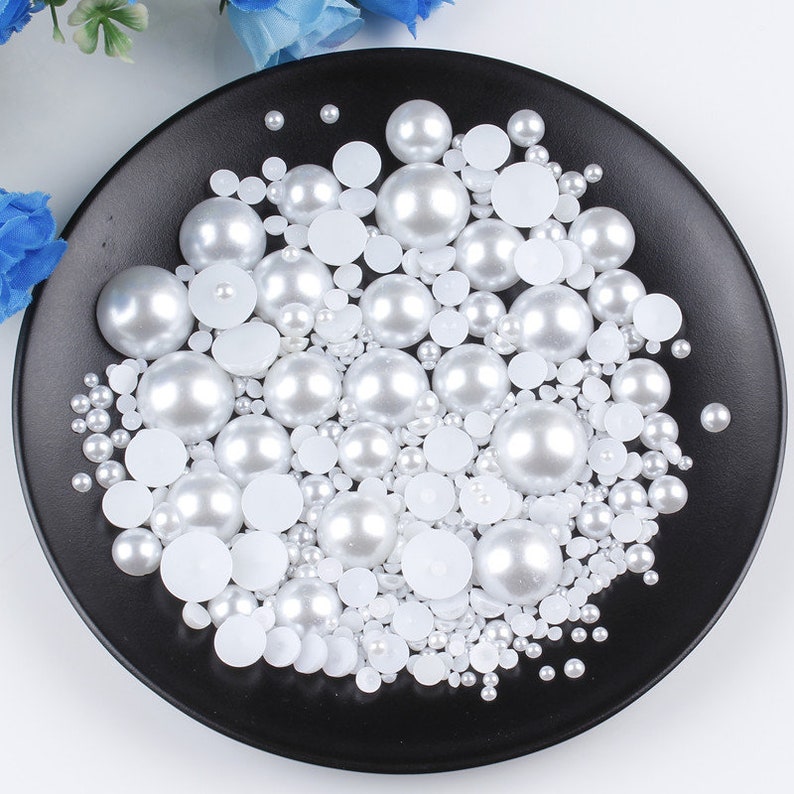 May include: A black plate filled with white pearl beads of various sizes. The pearls are a mix of round and flat shapes.