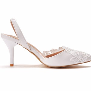 May include: White bridal heels with a delicate lace design on the toe and ankle strap. The heels are approximately 7.5 cm tall.