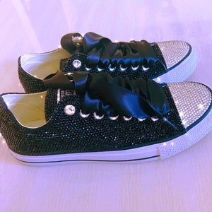 Pu&ograve; includere: Sneakers in tela nera con suola bianca e lacci in nastro di raso nero. Le sneakers sono ricoperte di strass neri e hanno un accento di strass argentato sulla punta.