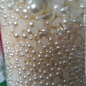 May include: A clear glass jar filled with a variety of white pearl beads and white plastic beads. The beads are of different sizes and shapes.