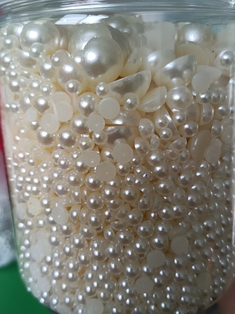May include: A clear glass jar filled with a variety of white pearl beads and white plastic beads. The beads are of different sizes and shapes.