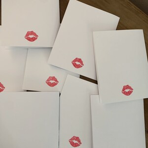 May include: A stack of blank white cards with a red lipstick kiss mark on each card.