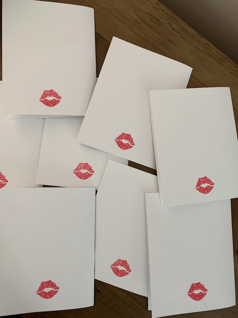 May include: A stack of blank white cards with a red lipstick kiss mark on each card.