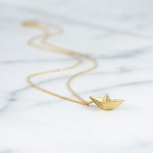 May include: A gold chain necklace with a small, origami paper boat pendant.