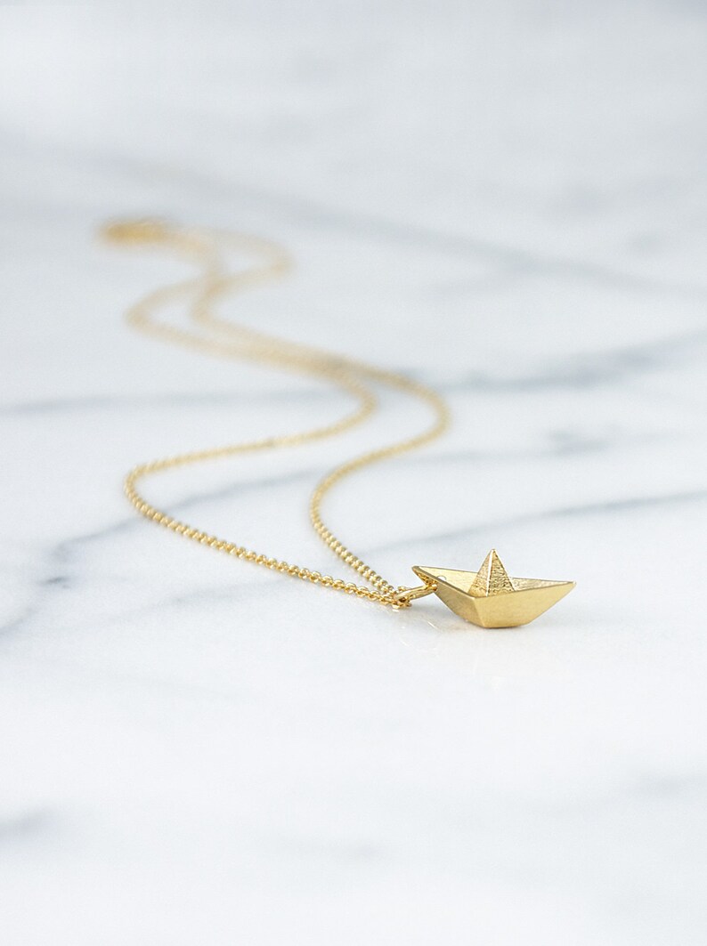 May include: A gold chain necklace with a small, origami paper boat pendant.