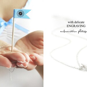 May include: A silver necklace with a small paper boat pendant. The pendant is engraved with the name "Konrad" and the date "16.11.2014".