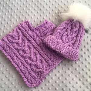 Peut inclure: Un ensemble de bonnet et écharpe en tricot violet avec un pompon blanc sur le bonnet.