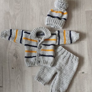 May include: A gray knitted baby outfit with yellow and blue stripes. The outfit includes a cardigan, pants, and a hat with a pom-pom.