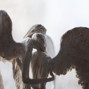 May include: Three white plaster angels with wings, sculpted in a pose of embracing each other.