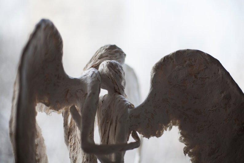 May include: Three white plaster angels with wings, sculpted in a pose of embracing each other.
