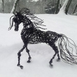 Puede incluir: Una escultura de alambre negro de un caballo de pie en la nieve. El caballo est&aacute; hecho de alambre delgado que est&aacute; retorcido y doblado para crear la forma del caballo. El caballo est&aacute; de pie sobre una superficie nevada.